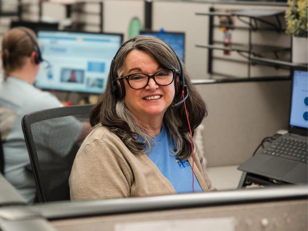 woman at a cubicle wearing a headset, smiling